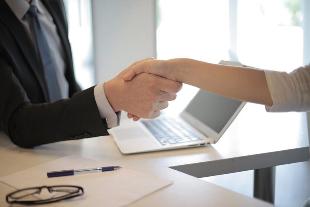 Two people shaking hands across a desk.