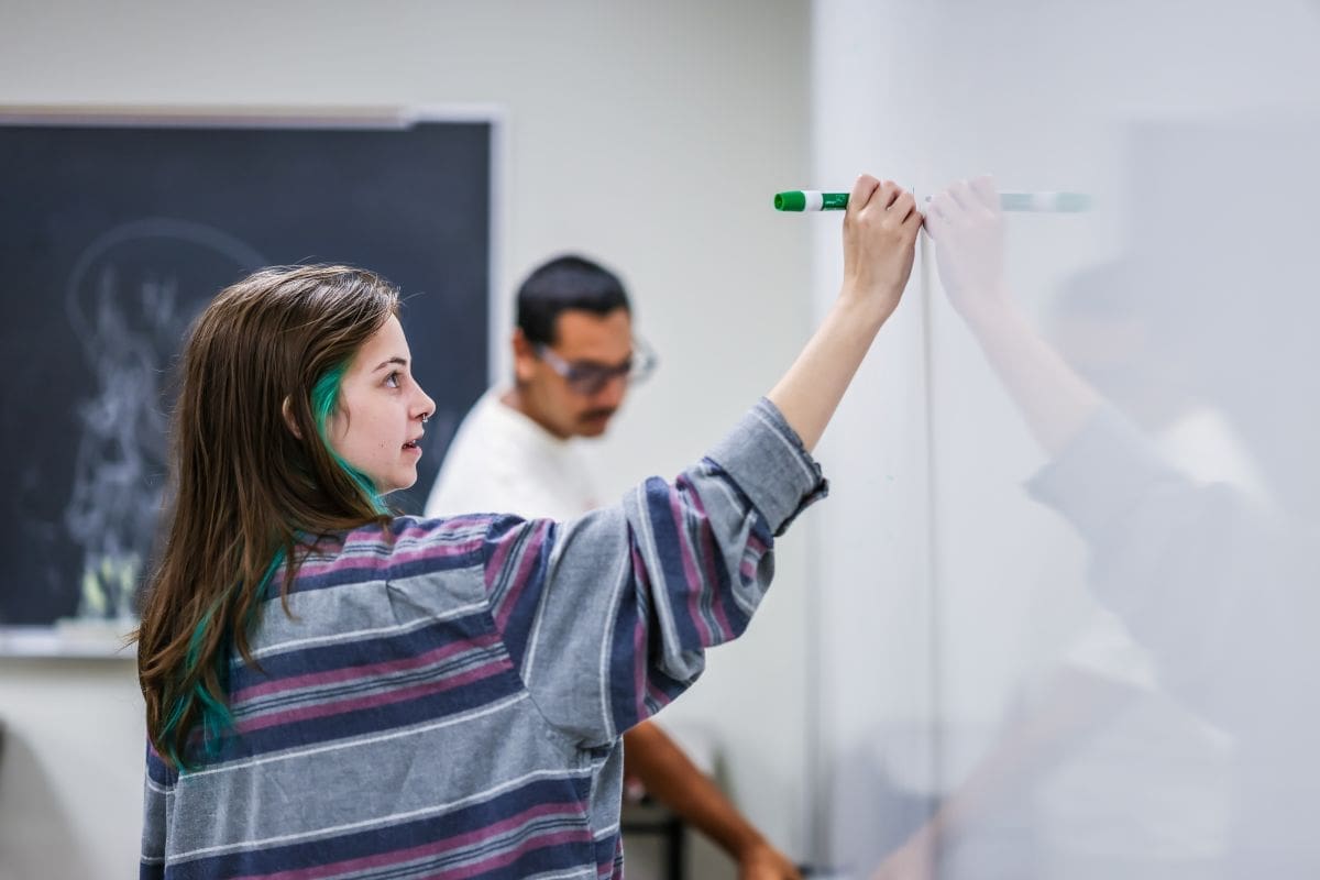 A student writing on a white board in a math class